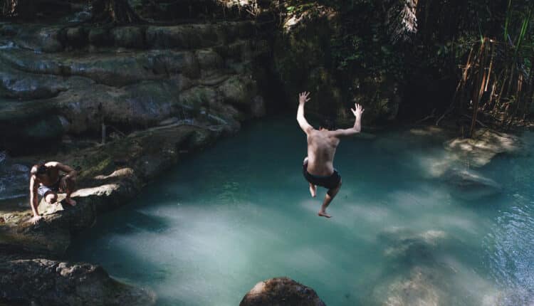 Outdoor adventure shot: someone diving around hidden islands into a clear natural pond in a wooded setting.